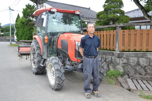 作業場のトラクターを前にした　松浦敏さん